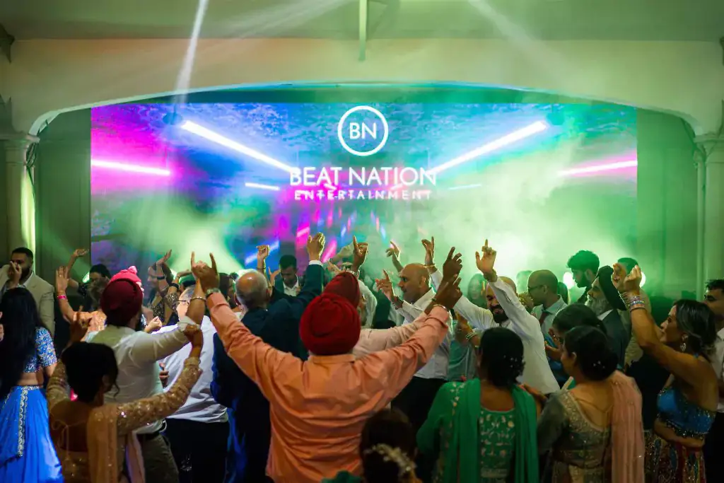 Wedding guests dancing with their hands up in front of a Beat Nation LED wall