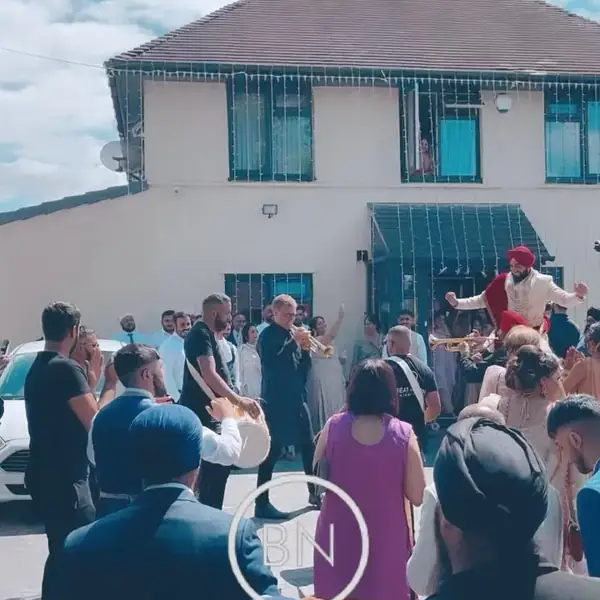A baraat arriving outside a house with a dhol player and guests